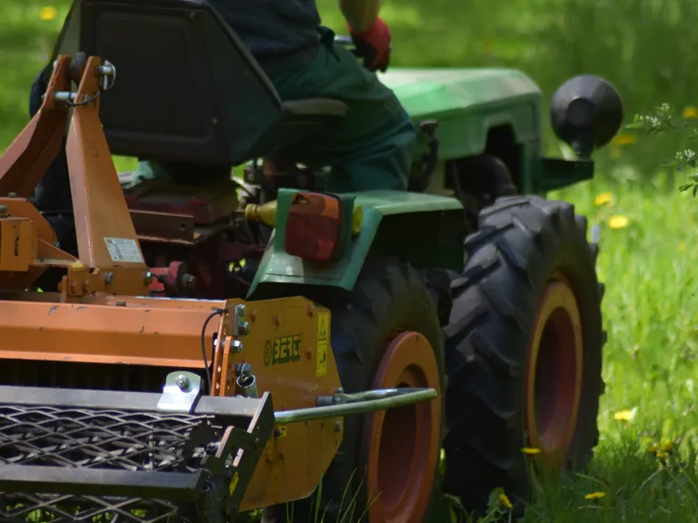 Tractor pulling a rotary cutter through tall grass and overgrown weeds