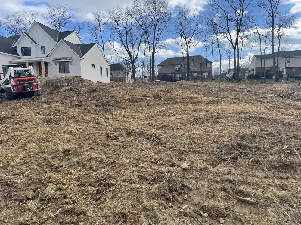 The same Maineville, OH lot graded flat beside a new build, skid steer on site