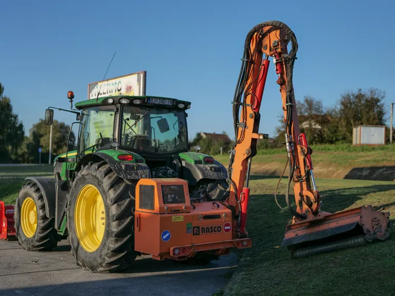 Tractor with a boom-mounted flail mower cutting back vegetation along a road corridor