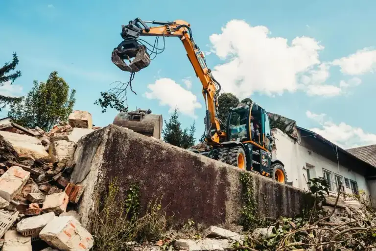 Excavator with a grapple attachment demolishing a small structure and clearing debris